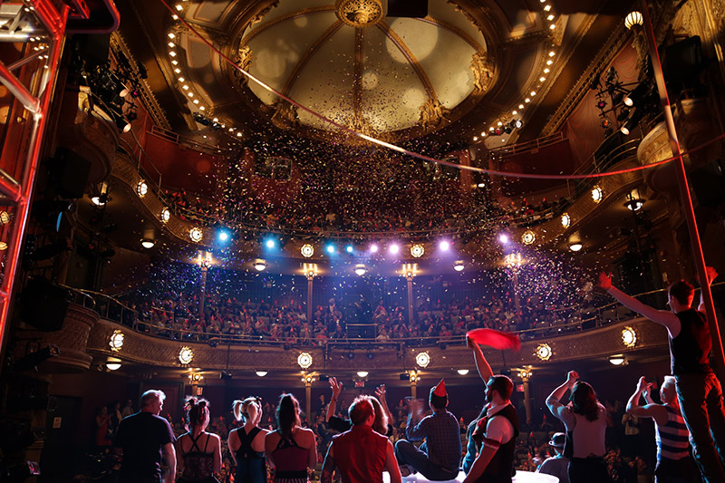 A theater audience celebrates New Victory's 20th Anniversary with confetti, festive lighting and streamers.